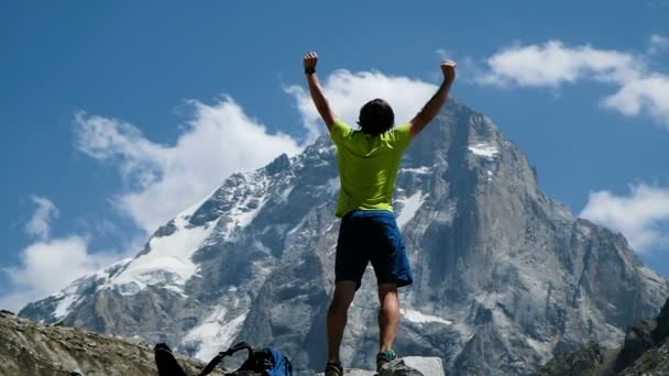 Man raises hand up in the mountains in a hike standing on a stone, a beautiful view opens up. Concept of victory and success, the achievement of the goal, slow motion - Footage, Video