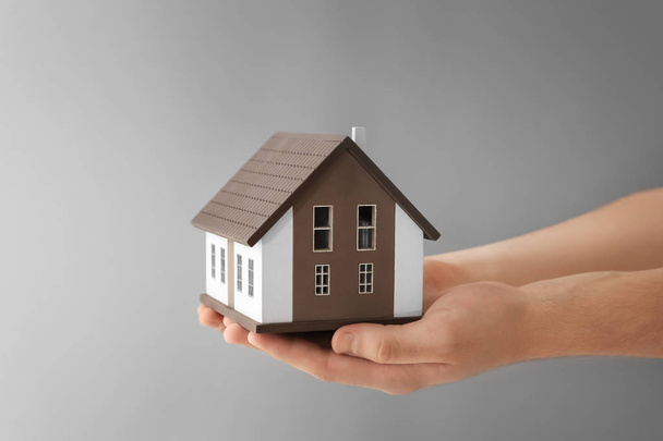 Man holding house model on grey background. Mortgage concept - Foto, Imagen