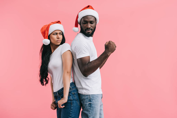 クリスマス帽子立っている背中合わせにピンクの背景で隔離のボーイ フレンドの怒っているアフリカ系アメリカ人女性  - 写真・画像