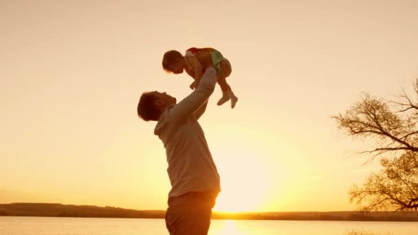 Dad plays with his daughter at sunset, raises his little daughter high up to the sky with his hands. Slow motion - Footage, Video