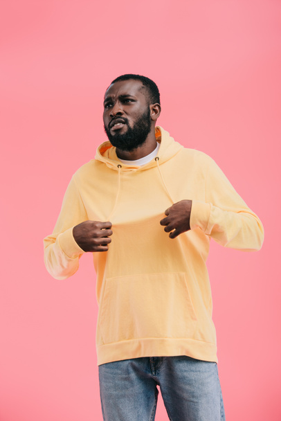 upset african american man showing yellow hoodie on himself isolated on pink background - Fotó, kép