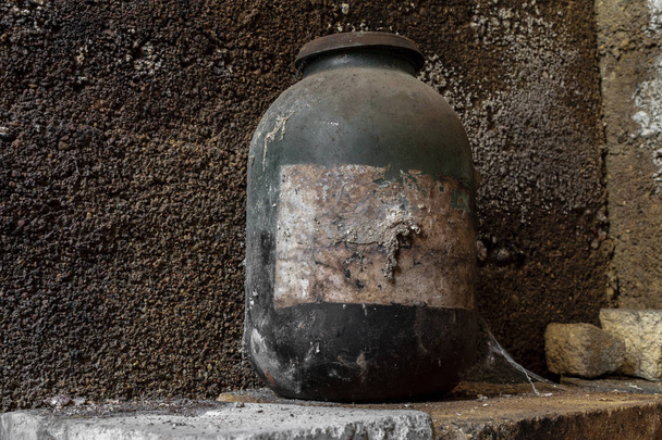 Very old and aged black jar covered with dust and spider web standing in front of the concrete wall at basement - Photo, Image