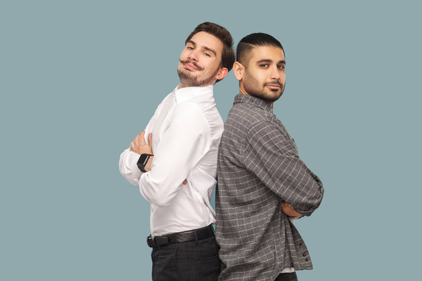 side view of two handsome bearded successful friends standing with crossed arms and looking at camera with proud face on blue background - Foto, Imagem