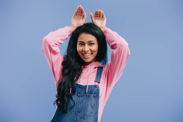 smiling young african american woman doing bunny ears by hands isolated on blue background  - Photo, Image