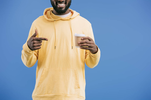 partial view of young african american man pointing by finger at disposable coffee cup isolated on blue background - Fotó, kép