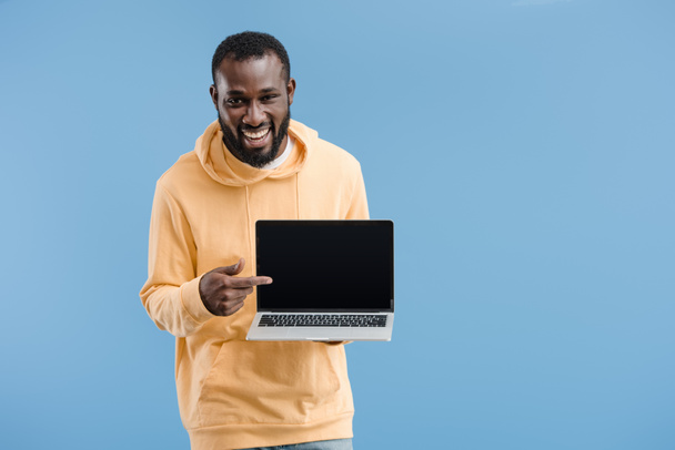laughing young african american man pointing by finger at laptop with blank screen isolated on blue background - Zdjęcie, obraz