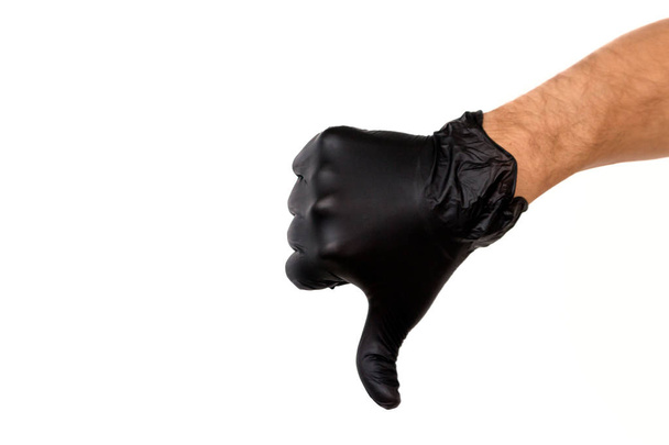 Isolate hand in a black rubber glove on a white background. Gesture thumb down or dislike. Concept of unsuccessful work of a chef of a surgeon or cleaning - Photo, Image