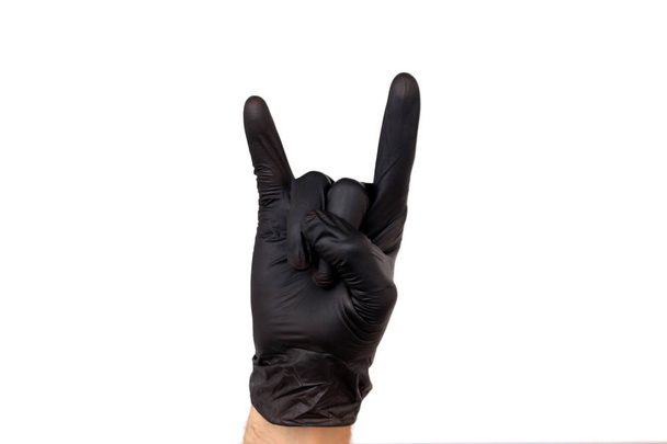 Isoleren hand twee vingers in een handschoen zwart rubber op een witte achtergrond te tonen. Penbeweging waarmee rotsen of horens. Het concept van de succesvolle werkzaamheden van een chef-kok van een chirurg of reinigen van schijven - Foto, afbeelding