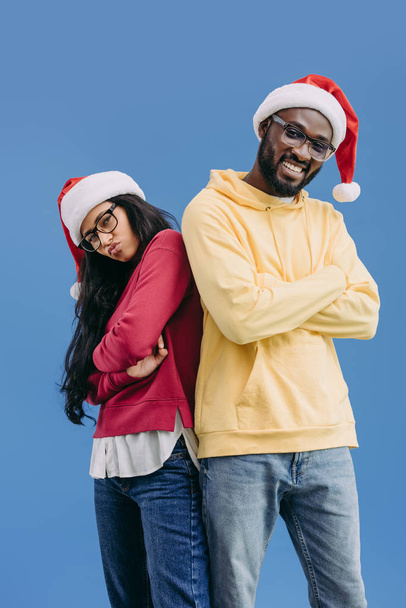 stylish african american couple in christmas hats standing with crossed arms isolated on blue background  - Φωτογραφία, εικόνα
