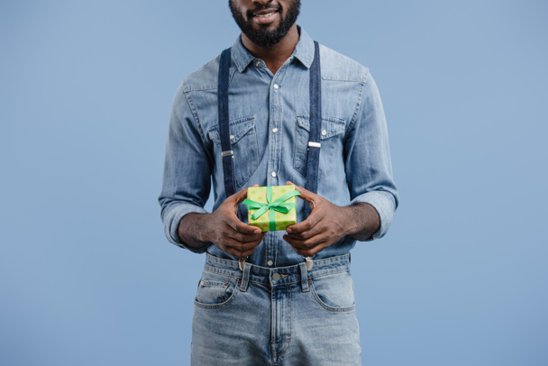 partial view of young african american man with gift box wrapped by ribbon isolated on blue background - Valokuva, kuva