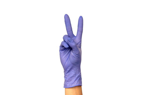 Isoler la main en montrant deux doigts dans un gant de caoutchouc lilas sur fond blanc. Le geste de la victoire. Le concept de travail réussi d'un chef de chirurgien ou de nettoyage
 - Photo, image