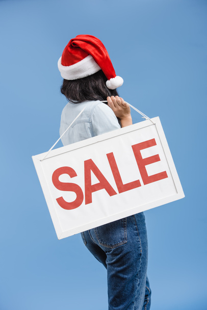 back view of african american girl in santa hat holding sale sign isolated on blue - Foto, imagen