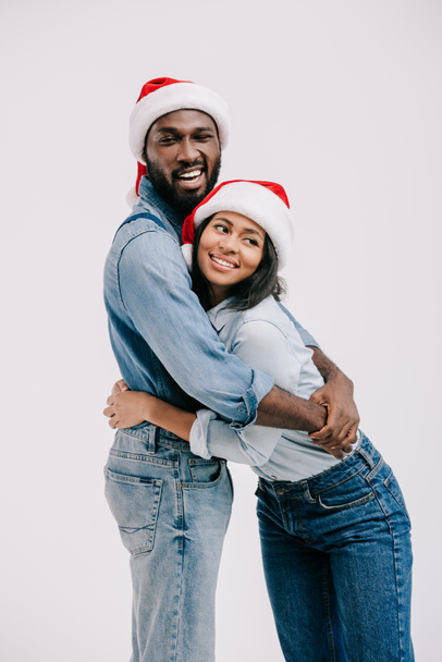 白で隔離を抱いてサンタ帽子でアフリカ系アメリカ人のカップルの笑顔 - 写真・画像