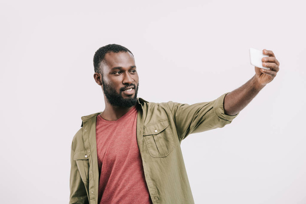 smiling handsome african american man taking selfie with smartphone isolated on white  - Фото, зображення
