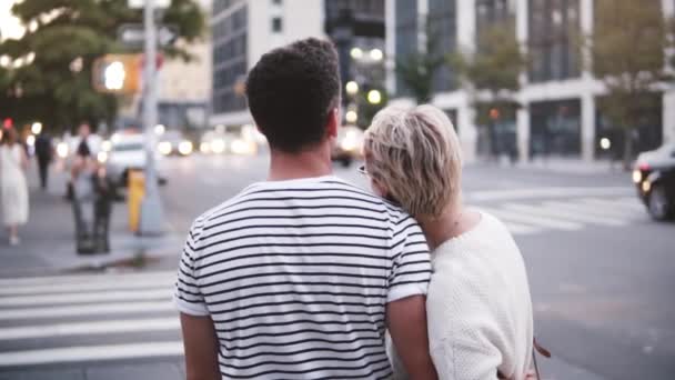 Slow motion smiling young Hispanic man hugging his Caucasian girlfriend near atmospheric New York summer street crossing - 映像、動画