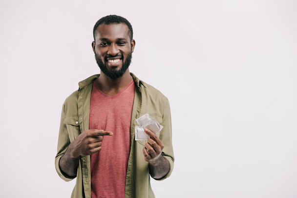 smiling handsome african american man pointing on condoms isolated on white - Foto, afbeelding