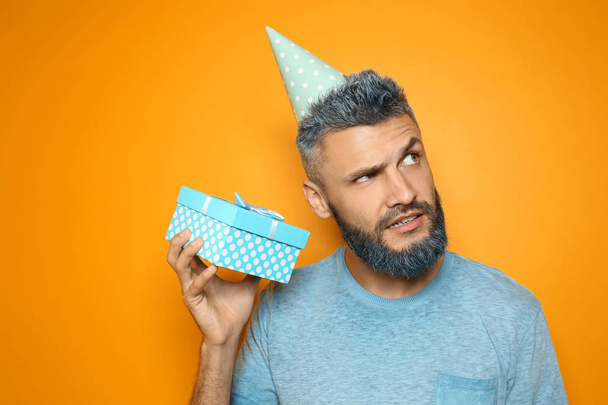 Portrait of emotional man with Birthday gift on color background - Valokuva, kuva