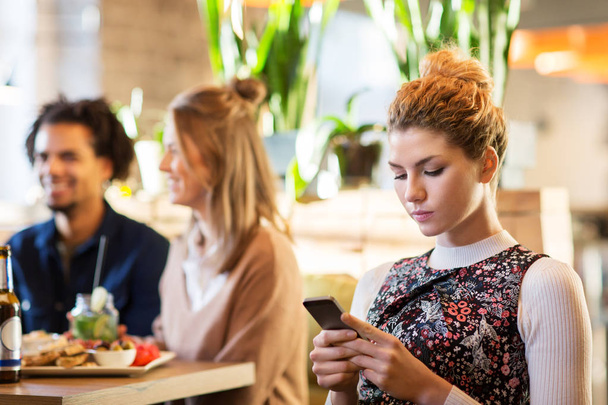 woman with smartphone and friends at restaurant - Foto, Bild