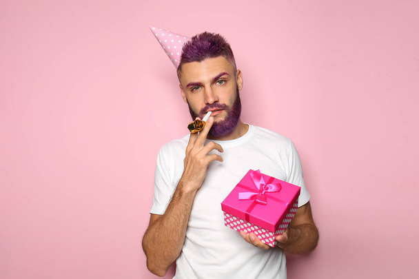 Porträt eines Mannes mit Geburtstagsgeschenk, Hut und Trillerpfeife auf farbigem Hintergrund - Foto, Bild