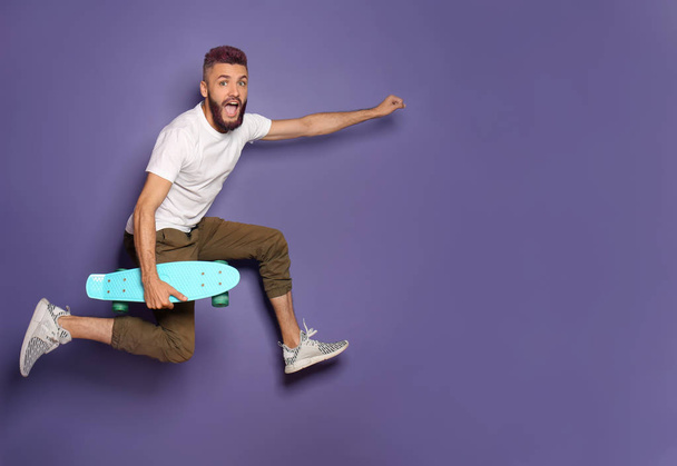 Active hipster with skateboard jumping against color background - Foto, afbeelding