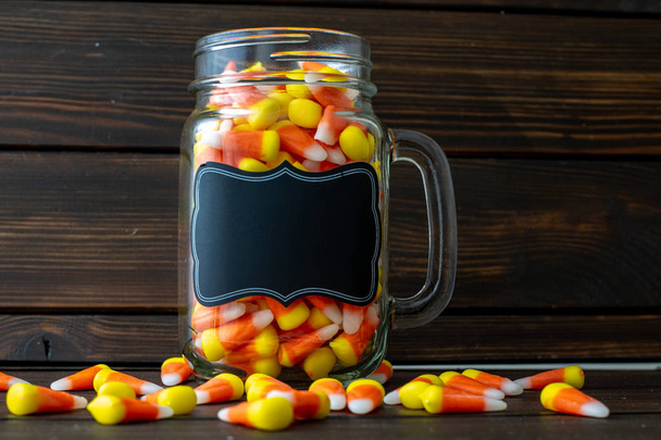 Cadre de fond Halloween composé d'un pot plein de maïs bonbon sur une table en bois sombre avec une table noire que vous pouvez personnaliser
. - Photo, image