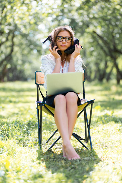 Business woman with a laptop in the Park sitting on a folding chair with her shoes in her hands - Fotoğraf, Görsel