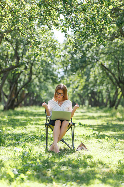Girl with laptop in the park sitting on a folding chair - Photo, image