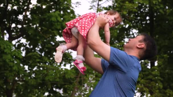 Le jeune papa et le bébé rient ensemble en jouant dehors. La fille saute dans l'air des mains des parents et sourit. Mouvement lent
. - Séquence, vidéo