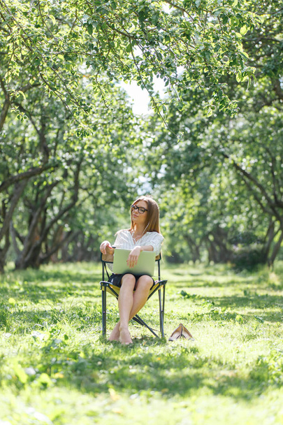 Girl with laptop in the park sitting on a folding chair - 写真・画像