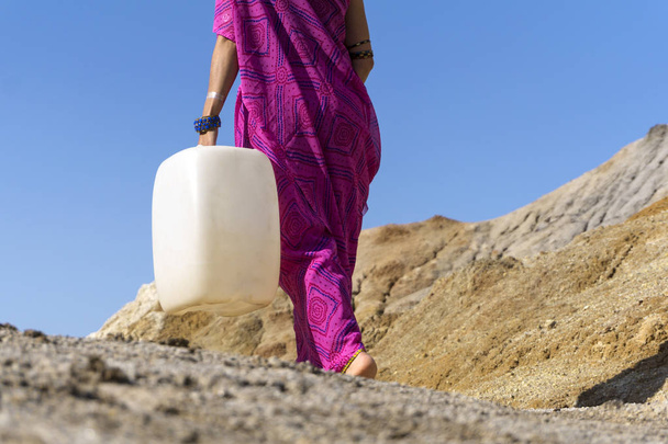 uma menina em roupas étnicas vai para a água com um jerrican plástico
 - Foto, Imagem