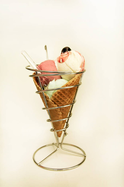 Власники морозива. Полуниця, м'ята, ваніль з кислим вишневим морозивом у великому вафельному конусі у тримачі, ложці. Свіжоспечене морозиво вафельний конус, що сидить на срібній підставці. магазин морозива. кондитерський магазин
. - Фото, зображення