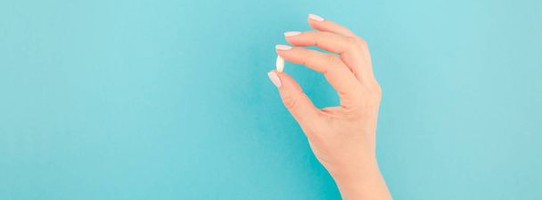 Woman hand holding a white pill on pastel blue paper background with copy space in minimal style, template for text. Concept of medical treatment, pharmacy, healthcare. Long wide banner - Photo, Image
