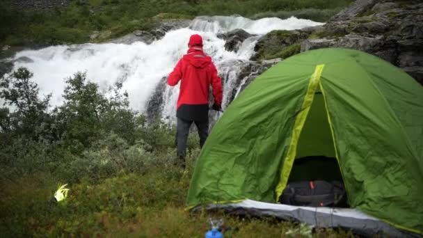 Kaukaski mężczyzn picie gorącej herbaty przed wodospad. Camping w dzikie tematu. - Materiał filmowy, wideo