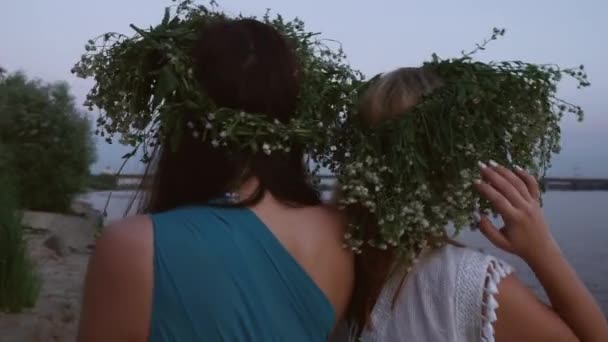 Two beautiful girls with wreaths on the head on the river bank - Кадры, видео