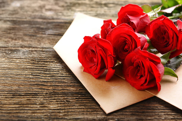 Beautiful bouquet of red roses and envelopes on wooden background - Foto, afbeelding