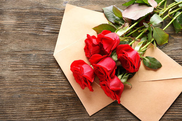 Beautiful bouquet of red roses and envelopes on wooden background - Fotó, kép