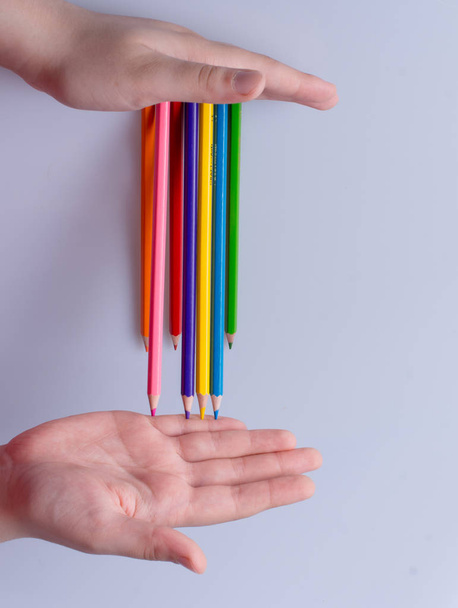 Рука тримає кольорові олівці, розміщені на білому тлі
 - Фото, зображення