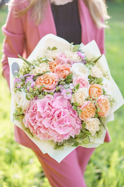 Mujer encantadora sosteniendo un hermoso ramo de primavera. arreglo floral con hortensias y rosas de jardín. Color rosa. césped verde en el fondo
 - Foto, Imagen