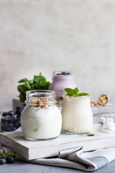 Jars with healthy yogurt with fresh blueberries, granola and mint. Tasty parfaits - Foto, afbeelding