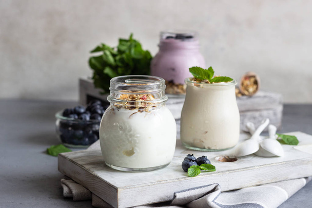 Jars with healthy yogurt with fresh blueberries, granola and mint. Tasty parfaits - 写真・画像