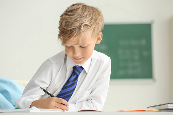 Милый маленький мальчик делает домашнее задание в классе
 - Фото, изображение