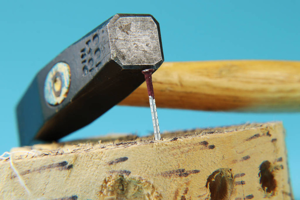 Un petit marteau de fer avec un bâton de bois et un clou de rouille dans la planche de bois. Fond bleu
 - Photo, image