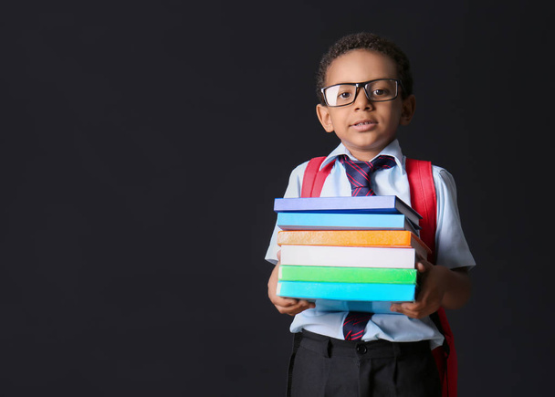 Funny African-American schoolboy with books on dark background - Photo, Image