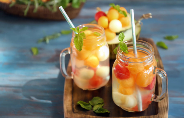 Mason jars of delicious cocktails with melon balls on wooden board - Photo, image