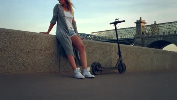 Attractive woman with a scooter stands on the waterfront - Filmagem, Vídeo
