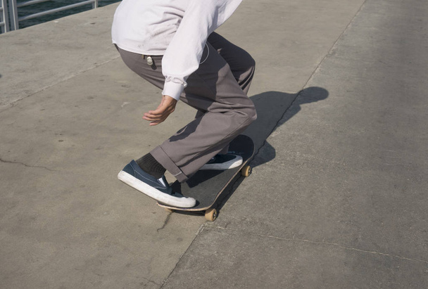 Young male skates low on a pier - Φωτογραφία, εικόνα
