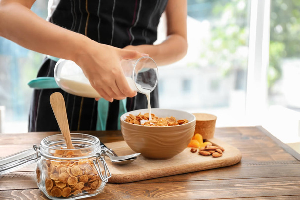 Woman pouring milk into bowl with corn flakes at table - Photo, Image