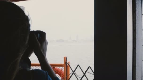 Silhouette of young tourist woman on boat trip to Statue of Liberty, New York taking photos with a camera on cold day. - Filmagem, Vídeo