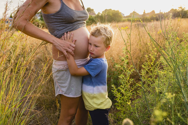 Παιδί αγκάλιασε η έγκυος μητέρα στο ηλιοβασίλεμα. - Φωτογραφία, εικόνα