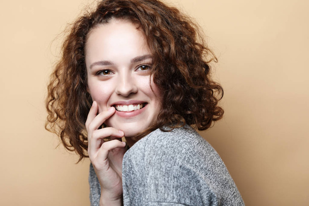 People, happiness and facial expressions concept. Pretty young curly woman with cute smile poses alone against beige background. - Foto, imagen